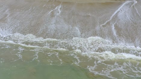 La-Cámara-Captura-La-Belleza-De-Una-Playa-Tropical-Desde-Arriba,-Moviéndose-Lentamente-Hacia-Abajo-Para-Mostrar-El-Sorprendente-Contraste-De-La-Espuma-Blanca-Y-El-Agua-Turquesa-Cuando-Las-Olas-Rompen-En-La-Orilla-Arenosa