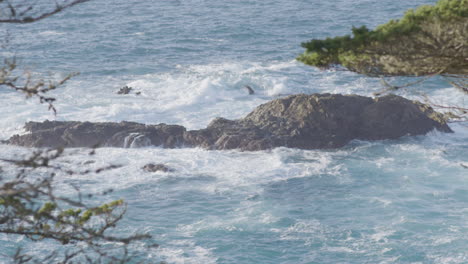 Stationary-shot-of-Pacific-ocean-waters-crashing-against-rocks-on-a-sunny-day-located-at-Big-Sur-California