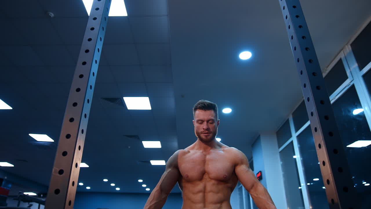 Shirtless male athlete walks to the horizontal bar for training. Selective focus on bodybuilder. Slow motion.