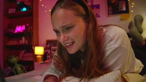 young woman laughing while using her laptop in bed