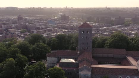 Clockwise-aerial-orbit-of-The-Cloisters-in-Upper-Manhattan-NYC-in-hazy-morning-summer-sunlight-over-many-uptown-neighborhoods