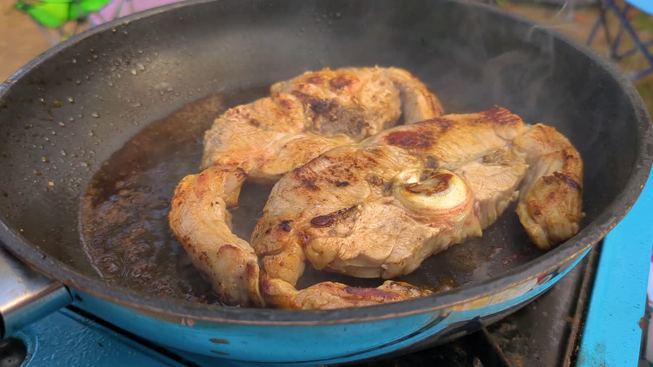 Sizzling Pork Chops Cooking Outside in Slow Motion with Steam Rising as Butter Melts. Cooked on Portable Gas Stove Camping in Great Outdoors 4K