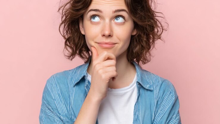 Contemplazione e Curiosità: Una Giovane Donna Pensierosa con Capelli Ricci che Riflette su un'Idea su uno Sfondo Rosa Tenue