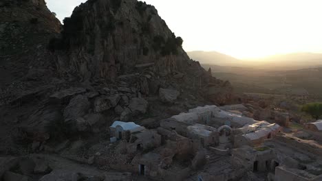 Aerial-shot-flying-forwards-over-the-ancient-village-that-is-sitting-in-the-shade-of-the-valley-during-a-beautiful-and-peaceful-sunset