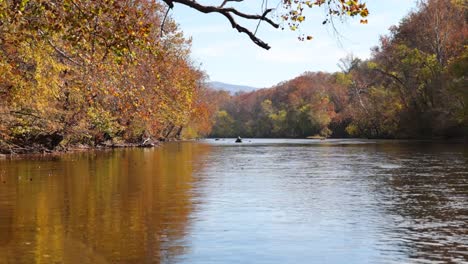 Push-in-shot-floating-down-river-in-autumn-with-other-kayakers-ahead