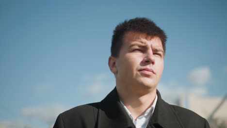 close-up of investor walking confidently outdoors wearing elegant black coat, surrounded by modern urban buildings, blue sky, and blurred streetlights