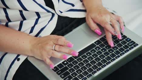 woman typing on laptop with vibrant pink nails, showcasing modern technology and creativity
