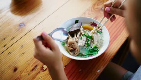 young woman eating thai chicken soup with rice noodles and greens at a street food cafe outdoors