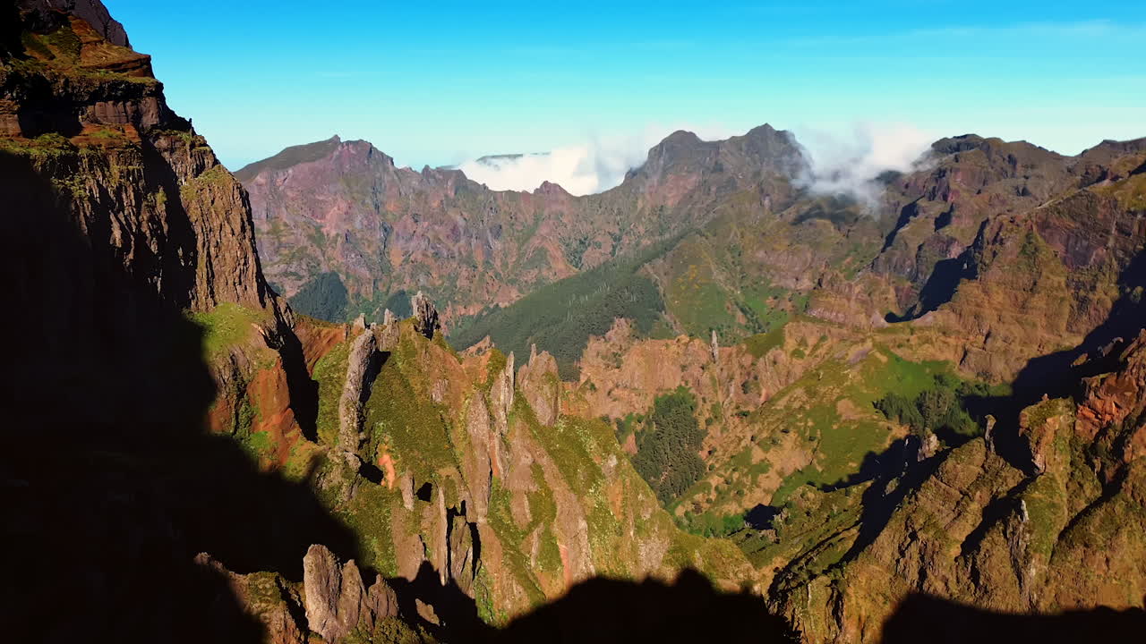 Dangerous high rocks with little greenery growing on. Cloudscape appears from behind the mountains. Madeira Islands, Portugal. Aerial view.