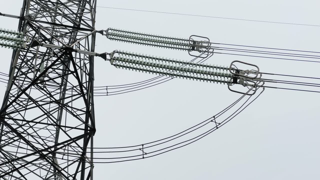 Panning shot capturing high-voltage transmission lines and insulators extending from a steel lattice electricity tower, emphasizing linear structure, engineering detail, and electrical infrastructure