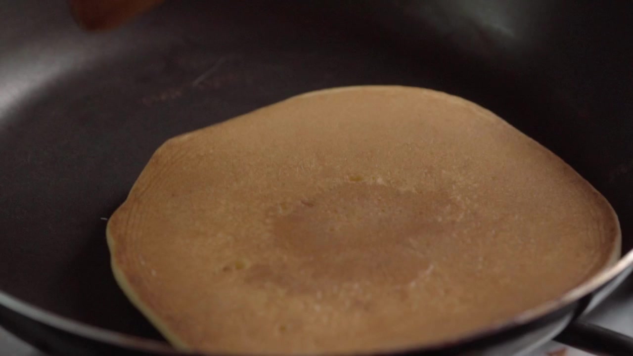Close-up de panqueca cozinhando em frigideira antes de virar. Bolhas de ar se formando na superfície da massa durante o preparo do café da manhã, mostrando o processo de cozimento caseiro.