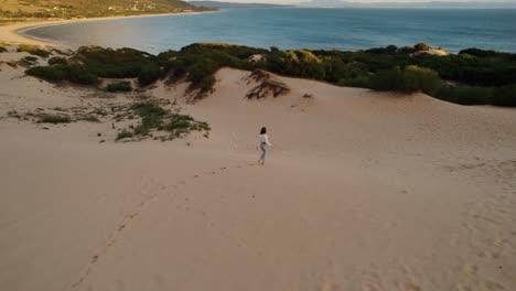 Drone-shot-of-a-young-woman-walking-through-the-sand-dunes-on-Spain's-coast