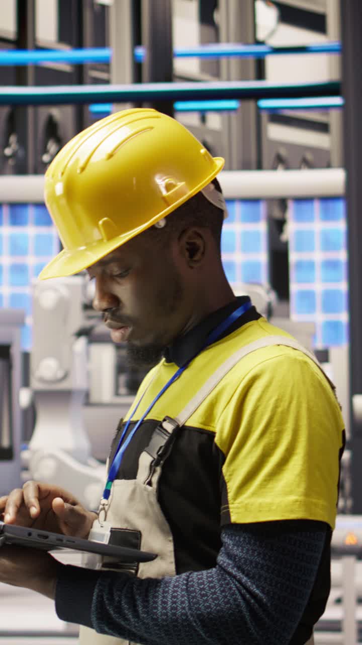 Vertical video Technician in solar panels factory oversees robot assembly lines using laptop