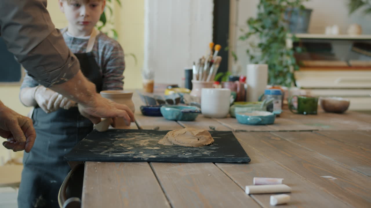 Child learning pottery from an adult instructor