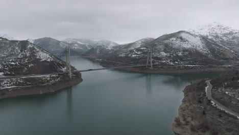 Ein-Fluss-Zwischen-Einem-Gefrorenen-Gebirgstal-Und-Einer-Brückenstraße,-Die-Zwischen-Dem-Stausee-Barrios-De-Luna-In-Leon,-Spanien,-über-Die-Infrastruktur-Von-Luftdrohnen-Führt