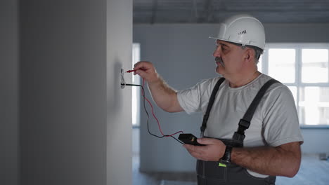 un hombre electricista comprueba el voltaje en la red con un probador de cables preparándose para instalar un hogar inteligente. inspección de todos los sistemas por un electricista profesional