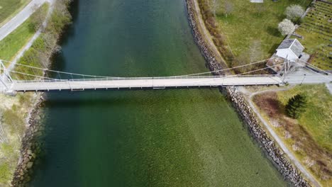 old suspension bridge over river in modalen norway - aerial fly over with tilt down