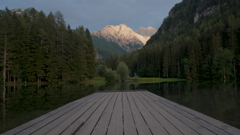 alpine mountain lake at sunset, plansar or plansarsko jezero in jezersko, slovenia, wooden pier extending above the water, tilt up revealing view