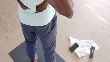 Mid-section-of-african-american-man-stretching-in-sunny-living-room,-slow-motion