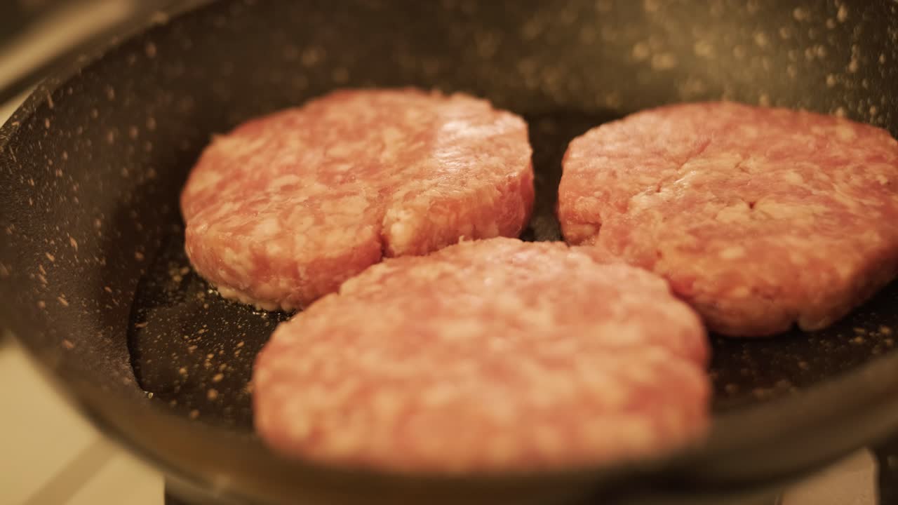 Raw meat patties frying in pan on kitchen stove