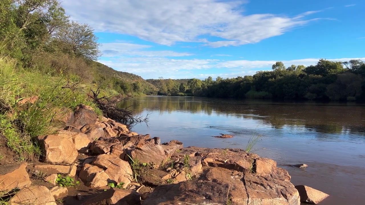 Vista dal basso lungo il fiume dalla riva. Il cielo blu presenta alcune nuvole