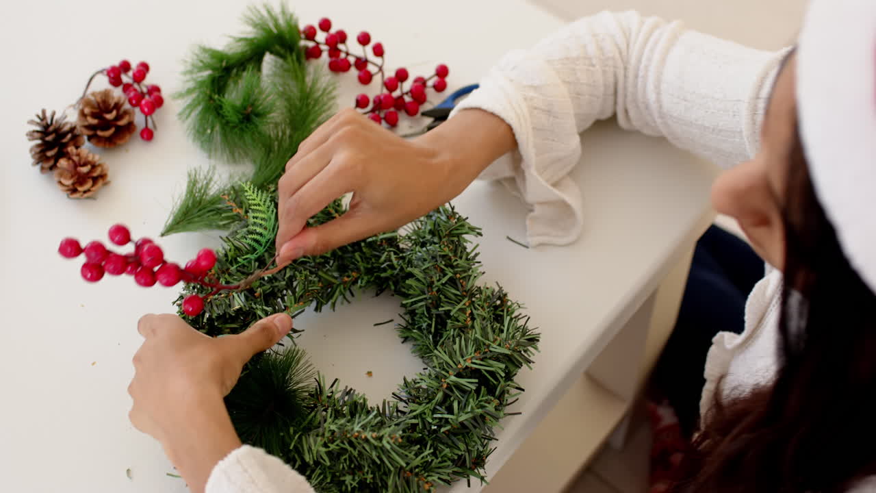 Indian woman crafting Christmas wreath with pinecones and red berries at home