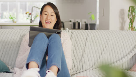 video of happy asian woman resting on sofa with tablet