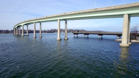 A-medium-shot-flying-above-the-Severn-River-with-ducks-taking-flight-by-the-Bridge