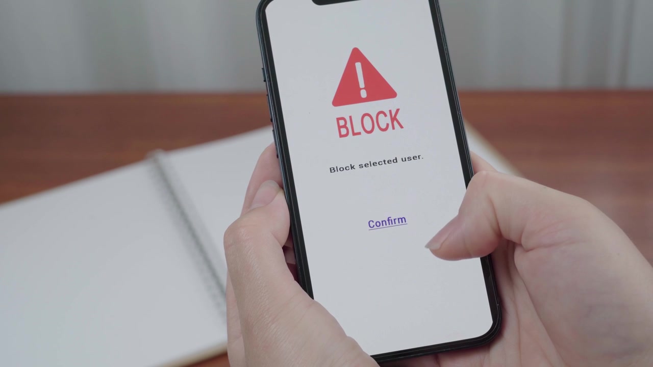 AI safety app displays a block selected user confirmation as a thumb hovers over the confirm link on a smartphone.