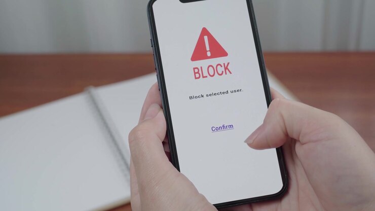 AI safety app displays a block selected user confirmation as a thumb hovers over the confirm link on a smartphone.