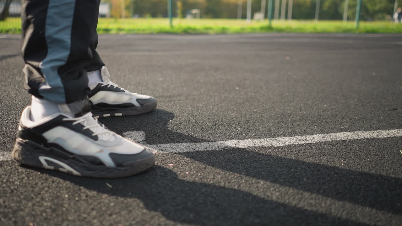 Primo piano sulle gambe di un atleta che indossa scarpe da ginnastica e pantaloni da jogging mentre palleggia con una pallavolo su un campo bianco, catturando il movimento, le calzature e la postura atletica in un ambiente sportivo all'aperto