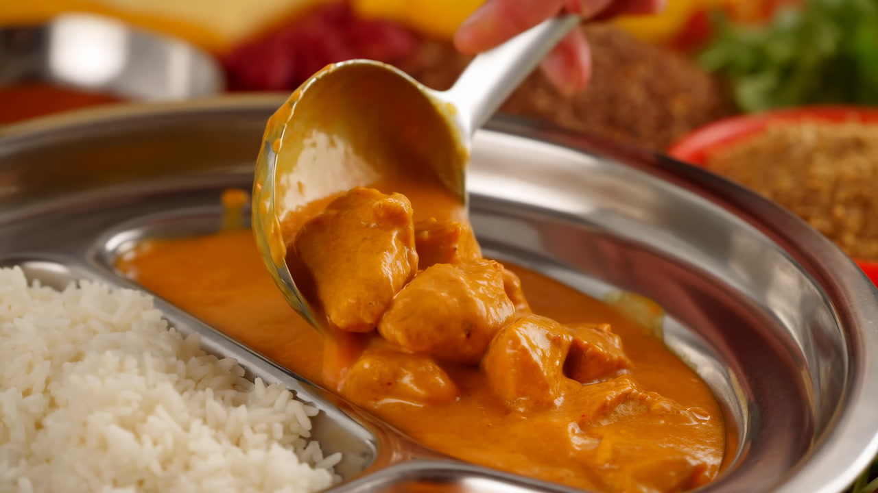 Ladling Orange Curry Sauce Over Rice, Closeup Of Server Spoon Pouring Creamy Butter Chicken Gravy Into Metal