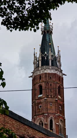 ornate spire of st. martin’s church rises behind treetops in landshut, germany, vertical closeup