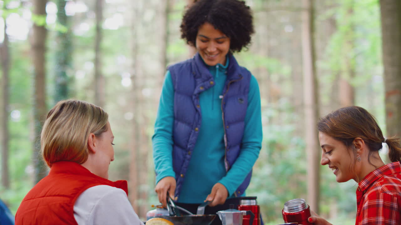 grupo de amigas en vacaciones de campamento en el bosque cocinando comida sentados en una tienda de campaña juntos