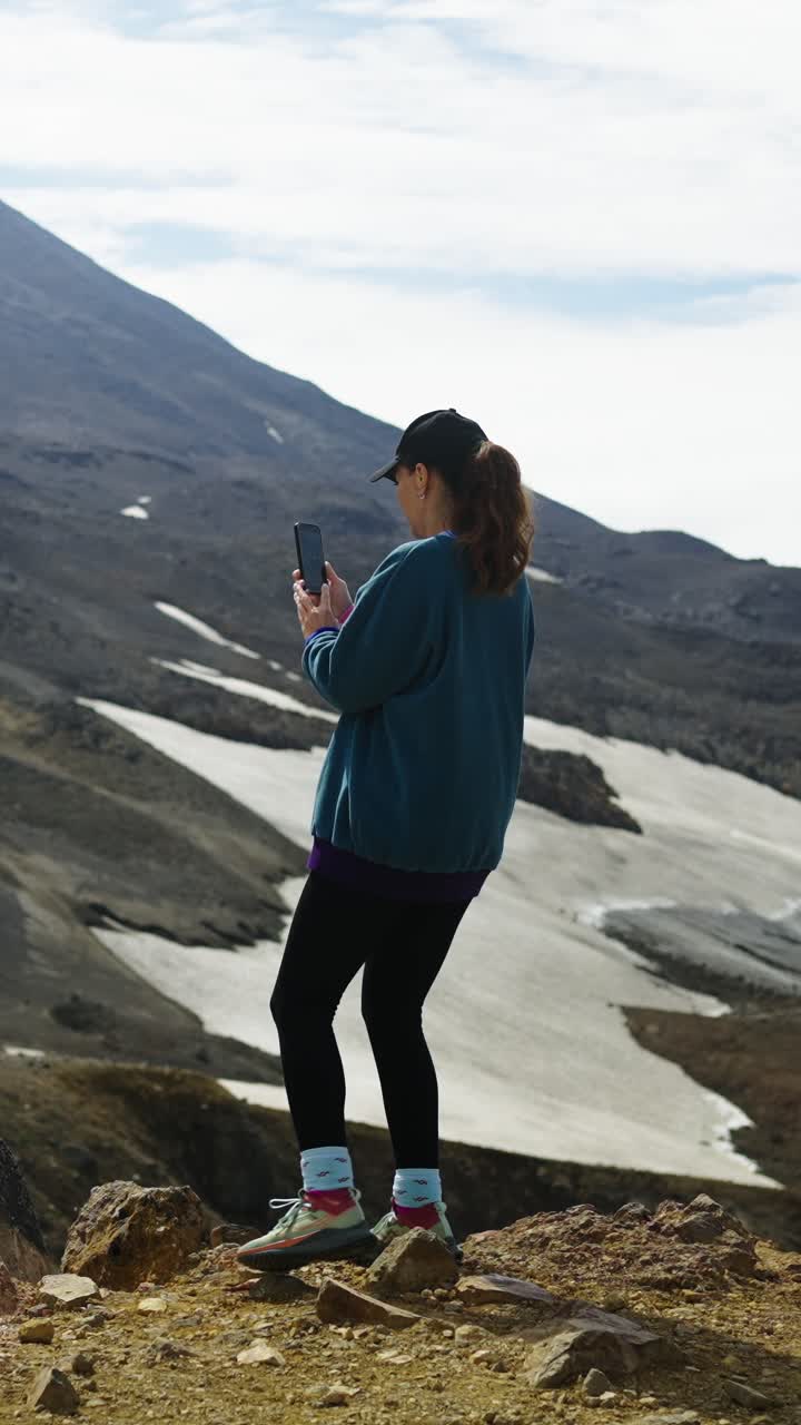Woman Standing on Mountain Taking Photo with Smartphone