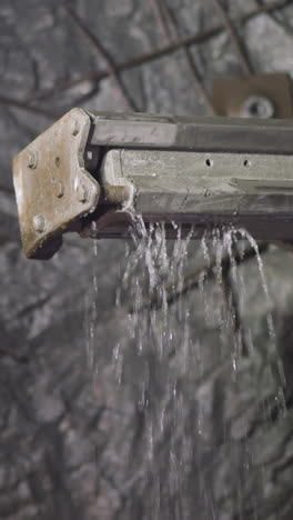 part of robot drill with cold water pouring down in ore mine. professional machinery equipment for drilling cavity and setting explosives closeup