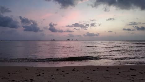 Fascinante-Toma-Estática-De-Pequeñas-Olas-Rompiendo-En-La-Playa-De-Arena-Durante-La-Hora-Dorada-Con-El-Cielo-Lleno-De-Color-Púrpura,-Tailandia