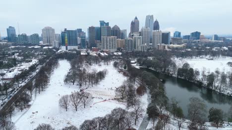 aerial push in on people sledding in a snow covered piedmont park with midtown atlanta in the background.
