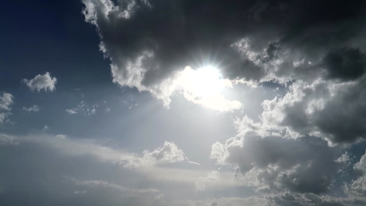 Bright sun peeking through large gray clouds in the blue sky