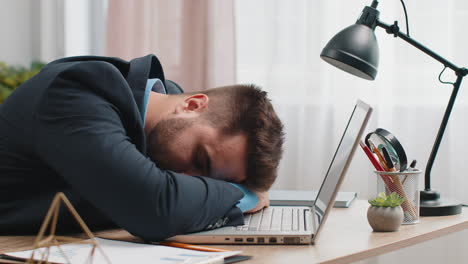 hombre de negocios caucásico aburrido trabajando en una computadora portátil, quedándose dormido en la oficina de casa