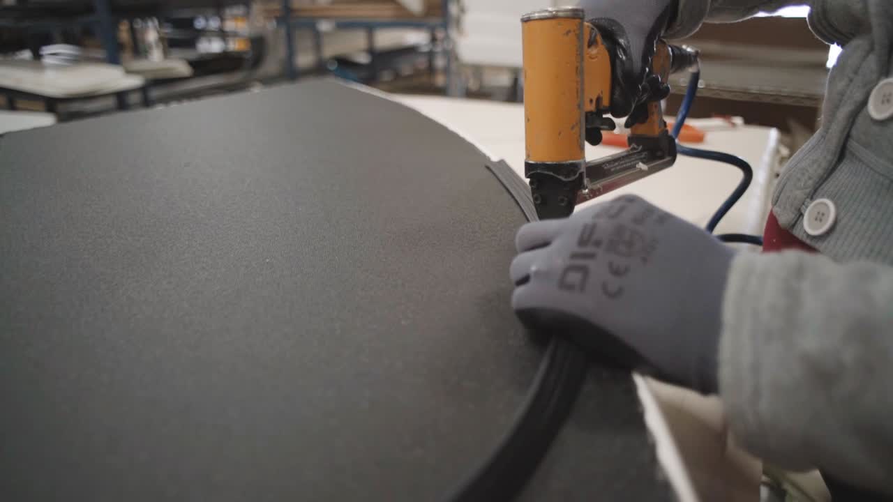 captura de pantalla de las manos de un trabajador calificado tapizando muebles con una pistola de clavos, taller interior