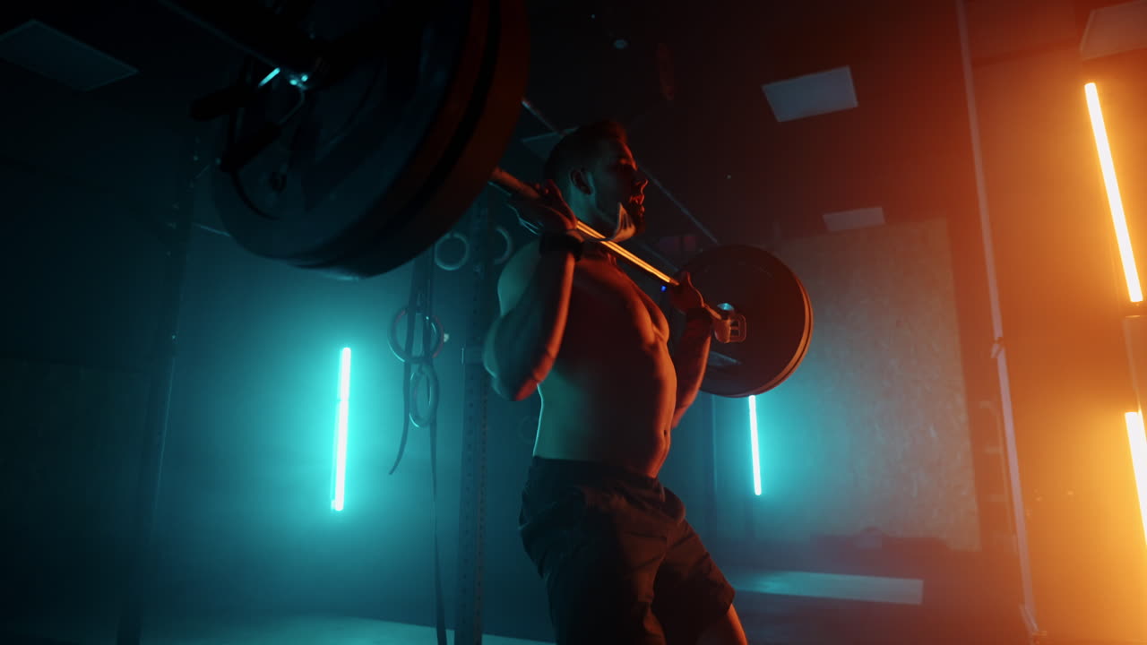 brawny powerlifter is training in gym lifting barbell in dark hall endurance and motivation