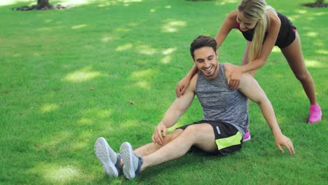 Una-Mujer-Deportiva-Ayuda-A-Su-Novio-A-Calentar-Antes-De-Hacer-Ejercicio-Al-Aire-Libre