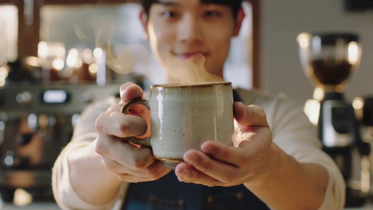 Barista con grembiule di jeans che offre una tazza fumante, servendo dopo la fine delle riprese al caffè.