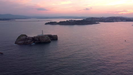 Dramática-Puesta-De-Sol-Aérea-Sobre-La-Ciudad-De-Santander,-El-Dron-Gira-Alrededor-De-La-Isla-Del-Faro-Vista-Panorámica-De-Toda-La-Bahía-Con-Playa-Y-Puerto