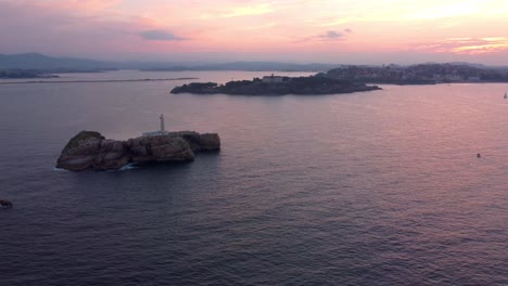 aerial dramatic sunset above santander city, drone rotate around lighthouse island panoramic view of all the bay with beach and harbor