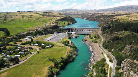 Blue-river-of-New-Zealand-with-small-town-and-concrete-dam,-aerial-view