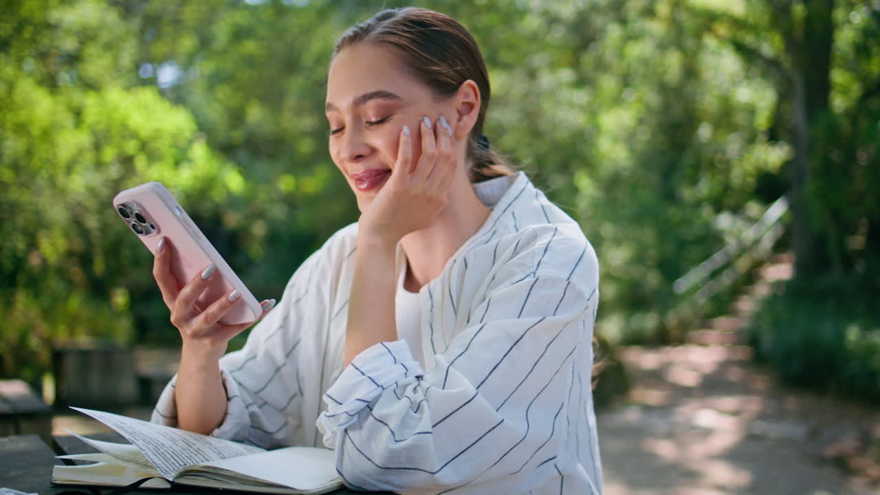 웃는 소녀가 드폰으로 메시지를 읽고 앉아 있는 공원 레크리에이션