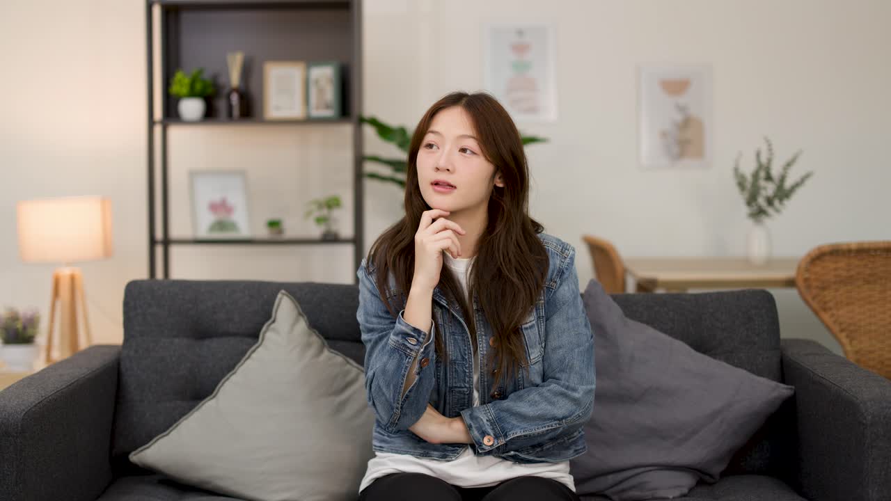 거실 소파에 앉아 생각에 잠긴 캐주얼한 젊은 여성, 은은한 실내 조명, 정적인 미디엄 샷