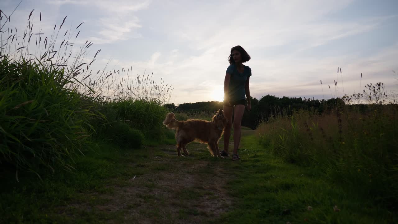 Woman walking with her golden retriever on a nature trail at sunset, peaceful mood